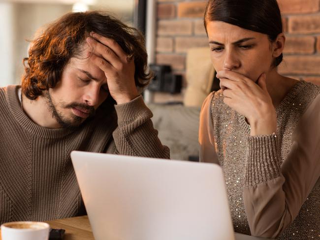 Young couple in a cafe using laptop for online banking and having problems with finances.