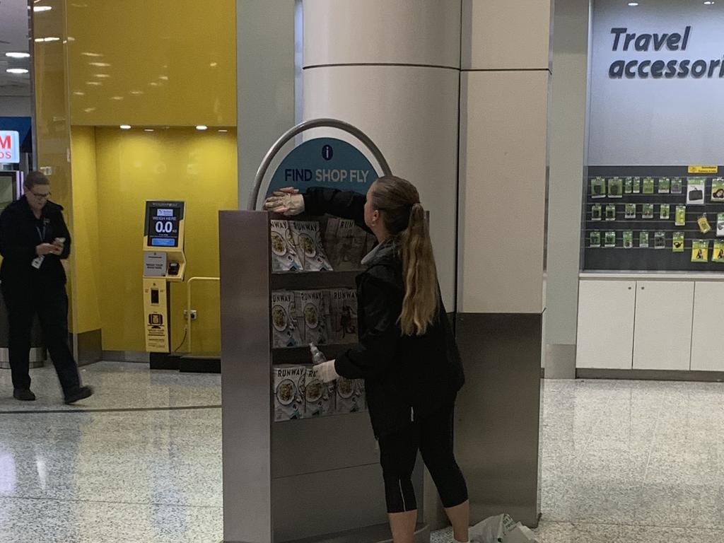 An airport worker sanitises an information board.