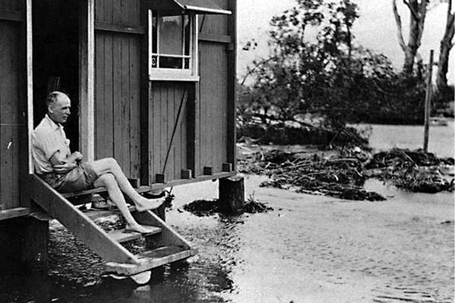 Man sitting on his house steps amidst flood waters at Moondarewa, South Stradbroke Island, Queensland, 1938