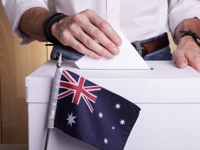 A man inserting a ballot to a ballot box. Australian flag in front of it.