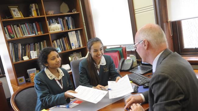 Students Shenaya Foran and Lorisa Reyes get stuck into some paperwork for principal Steve Walsh.