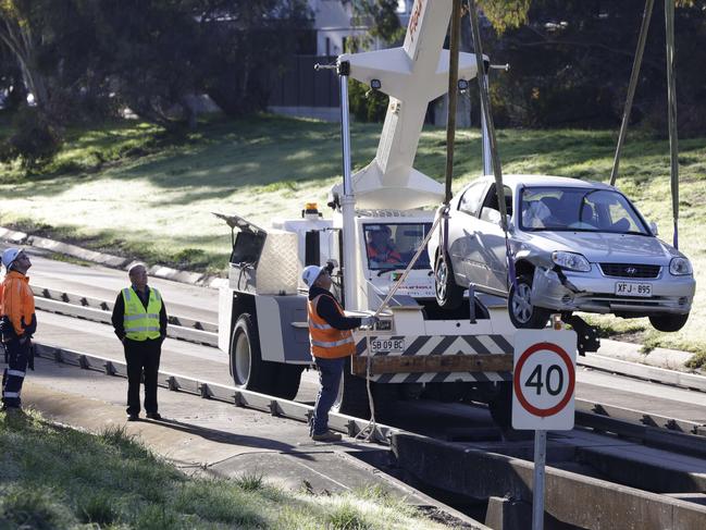 ADELAIDE, SOUTH AUSTRALIA - Advertiser Photos JULY 10, 2024: A crane and emergency workers lift a Hyundai sedan wedged on the outbound track after an 83-year-old women drove off the O-Bahn track at the Paradise Interchange, off Darley Road, this morning. Picture Emma Brasier