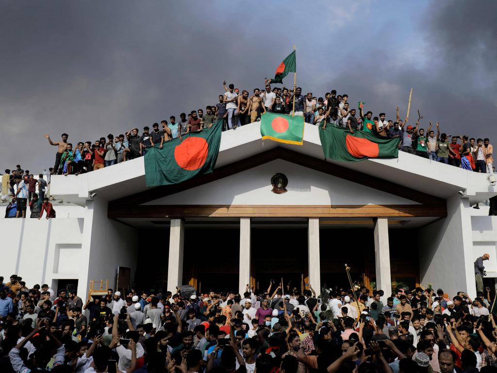 Anti-government protestors display Bangladesh’s national flag as they storm Prime Minister Sheikh Hasina’s palace in Dhaka on August 5, 2024.. Bangladesh army chief Waker-Uz-Zaman spent nearly four decades rising to the top of the military and said on August 5, he was “taking full responsibility” after Prime Minister Sheikh Hasina was ousted and fled. Picture: AFP