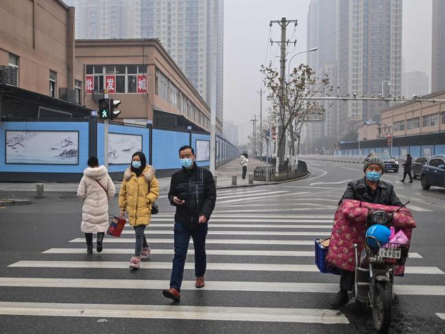 People cross a street in front of the closed Huanan Seafood wholesale market in Wuhan. Picture: AFP