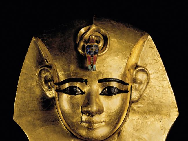 funerary mask of King Amenemopet-The king is shown wearing the nemes-headdress, with a uraeus formed from multiplesemiprecious stones at the forehead. Bronze forms the eyebrows, the outline of the eyes, the pupils, and the edge of the face. The mask was originally part of a wooden coffin. Ramses and the pharaohs gold exhibition, Australian Museum., with Christopher Allen story