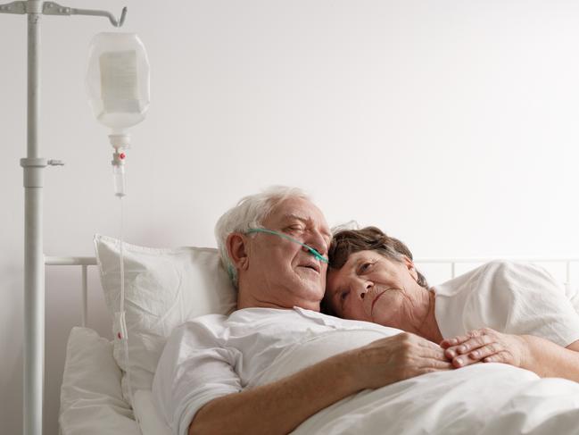 Shot of a sad wife lying next to sick husband at the hospital. Dying: istock