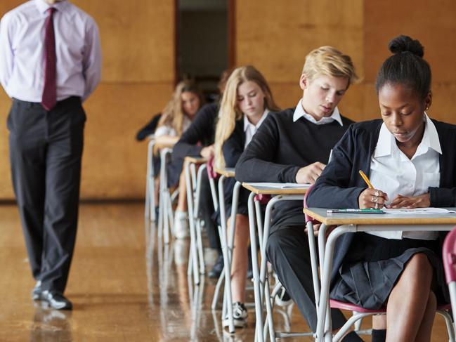 Teenage Students Sitting Examination With Teacher Invigilating