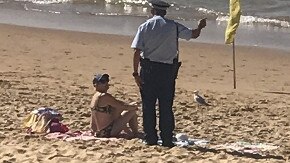 A police officer talks to a woman sitting on a towel at South Curl Curl Beach on Tuesday. Picture: Supplied