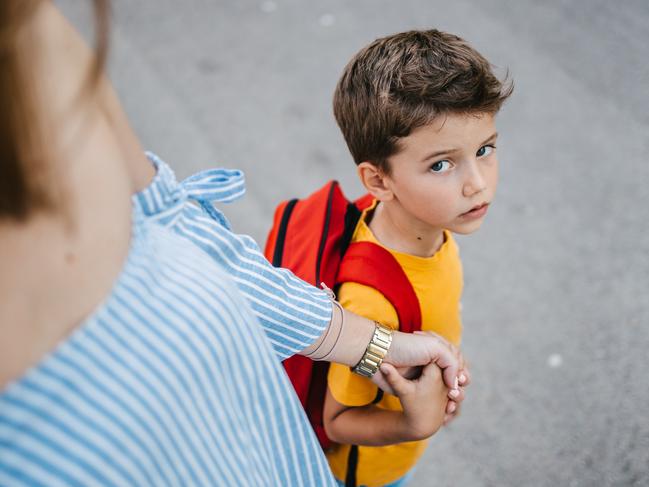 A son with a backpack and his mother holding his hand sending him to school on the first day of school and the schoolboy is looking at the camera