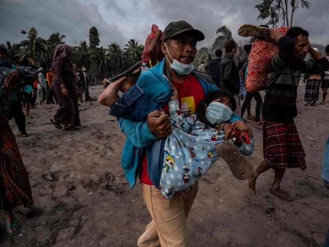 A villager carries a child as people salvage their belongings in an area covered in volcanic ash at Sumber Wuluh village in Lumajang. Picture: AFP