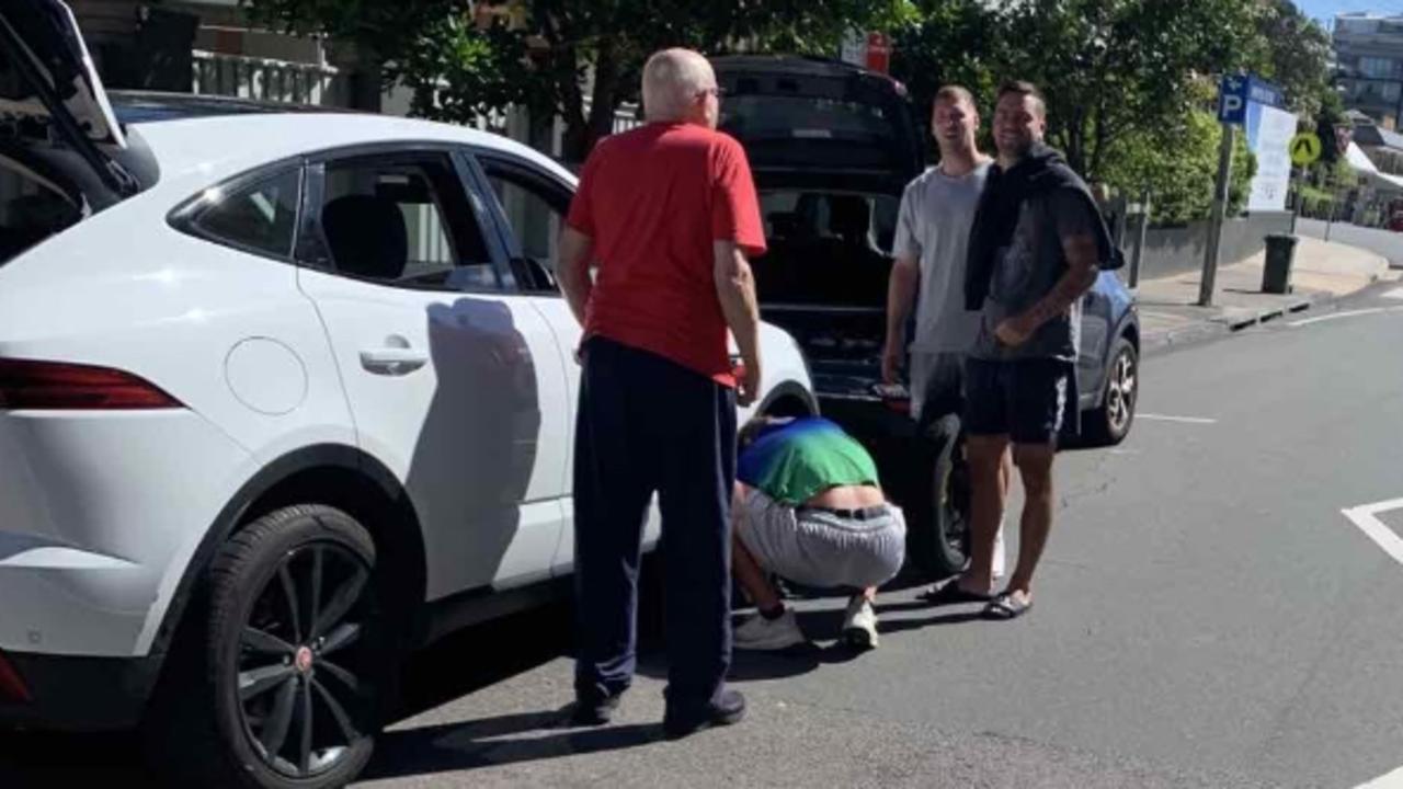 Warriors halfback Chanel Harris-Tavita changes a tyre for an elderly motorist on the Central Coast while teammates Bailey Sironen and Wade Egan watch on.