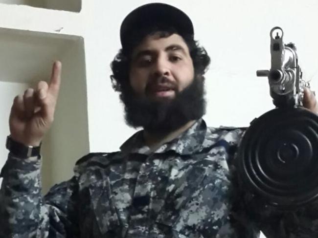 Clad in military fatigues, Sydney man Ahmed Merhi holds a large assault rifle while posing for a photo.