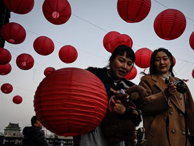 People walk past red lanterns at a rooftop cafe near the Drum Tower in Beijing on January 6, 2023. (Photo by Jade Gao / AFP)