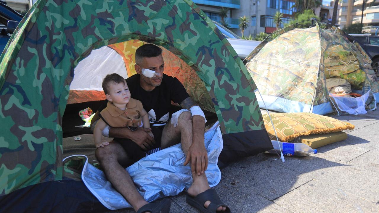 A wounded displaced man sits with his child inside their tent in central Beirut's Ain al-Mreisseh seaside promenade. (Photo by AFP)