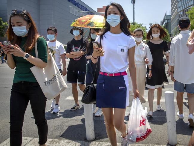 People wear face masks to protect against the coronavirus as they walk across an intersection in Beijing. Mask-wearing may become the ‘new normal’. Picture: AP Photo/Mark Schiefelbein