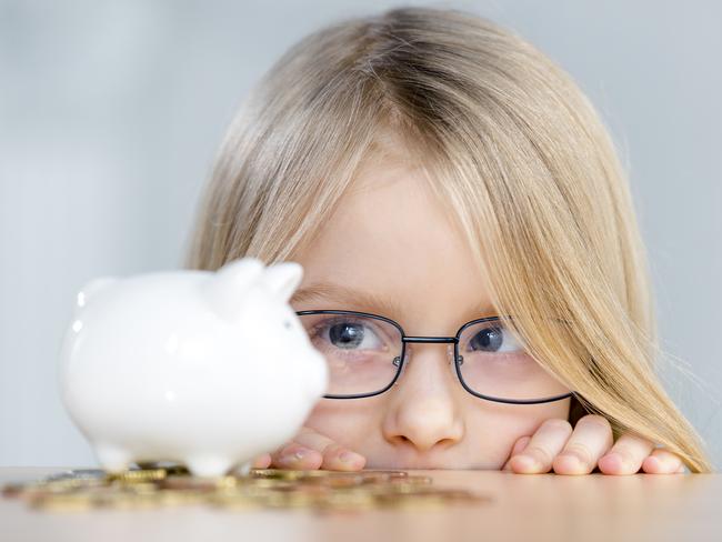 Cute little girl wearing eyeglasses looking at piggy bank