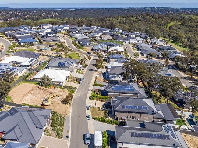 Aerial view of houses and streets in new wealthy suburb in Adelaide foothills with construction in foreground and coastline in background: large houses, landscaped gardens, rooftop solar systems,