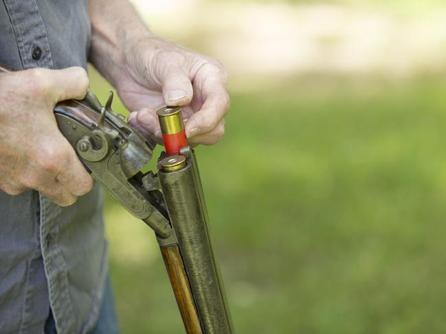 Senior Man loading an antique 12 gauge double barred shot gun. He is testing it prior to purchase or sell. He is outside, green grass in background.