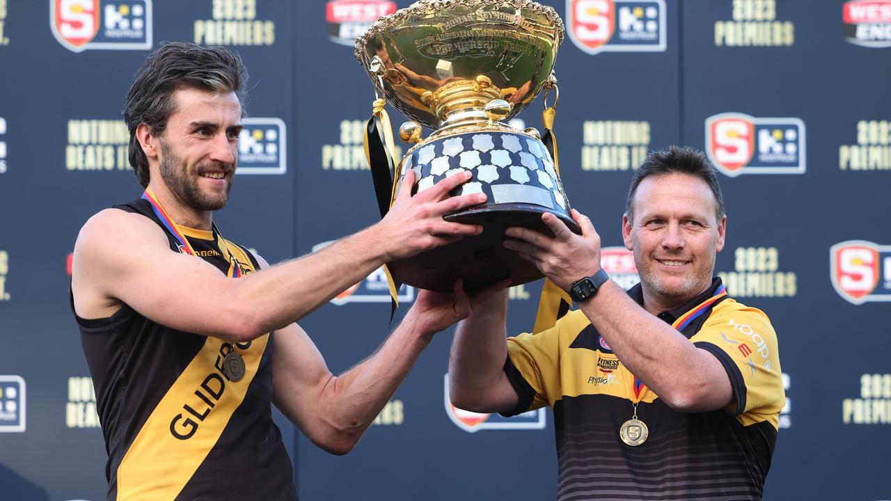 Max Proud (left) and Glenelg coach Darren Reeves hold the Thomas Seymour Hill premiership trophy aloft after Sunday’s grand final win against Sturt at Adelaide Oval. Picture: David Mariuz/SANFL