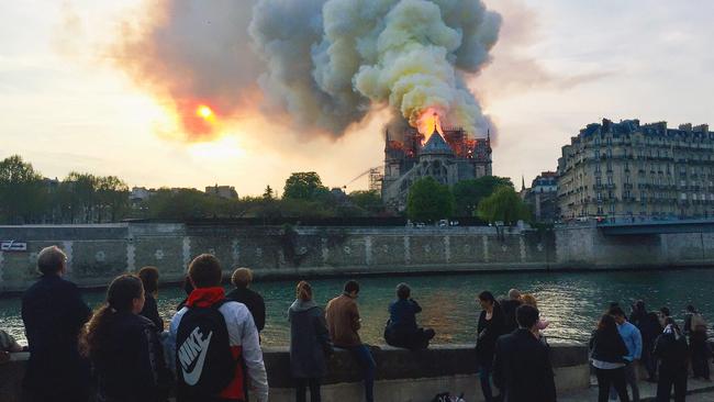 Bystanders watch flames and smoke billow from the roof of Notre Dame in Paris on April 15, 2019. Picture: AFP