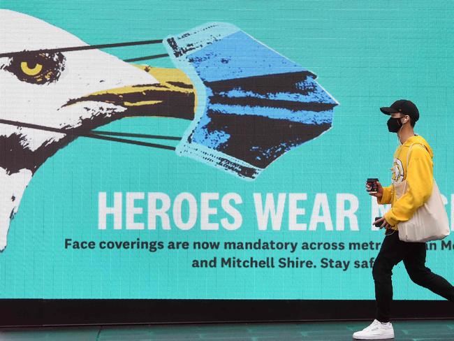 A man walks past a sign urging people to wear face masks in Melbourne on August 14, 2020 as the city battles an outbreak of the COVID-19 coronavirus. - The state remains effectively sealed off from the rest of the country, with other regions so far largely spared from new infections. (Photo by William WEST / AFP)