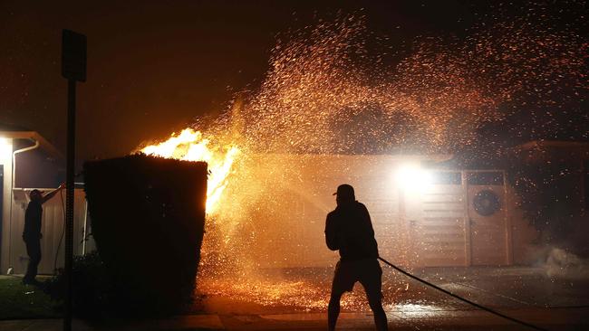 A person uses a garden hose to extinguish flames in front of a home as palm trees burn nearby during the Palisades Fire. Picture: Getty Images