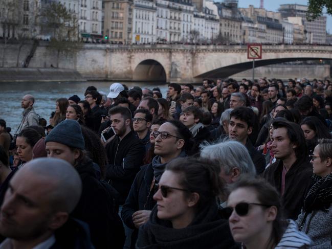 People watch as smoke and flames rising during a fire at the landmark Notre-Dame Cathedral in central Paris on April 15, 2019. - A huge fire swept through the roof of the famed Notre-Dame Cathedral in central Paris on April 15, 2019, sending flames and huge clouds of grey smoke billowing into the sky. The flames and smoke plumed from the spire and roof of the gothic cathedral, visited by millions of people a year. A spokesman for the cathedral told AFP that the wooden structure supporting the roof was being gutted by the blaze. (Photo by THOMAS SAMSON / AFP)