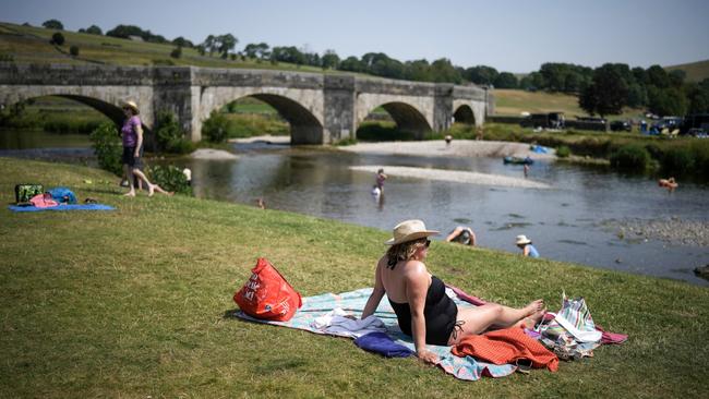 People relax in the hot temperatures and cool off in the River Wharfe in Burnsall, United Kingdom. Picture: Getty Images