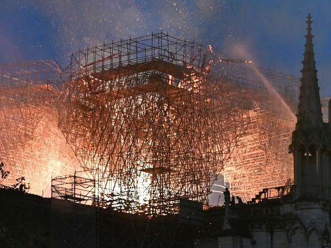 Flames are doused through the scaffolding erected on the roof of the Notre-Dame de Paris Cathedral after a fire broke out on April 15, 2019, in the French capital Paris. - A huge fire swept through the roof of the famed Notre-Dame Cathedral in central Paris on April 15, 2019, sending flames and huge clouds of grey smoke billowing into the sky. The flames and smoke plumed from the spire and roof of the gothic cathedral, visited by millions of people a year. A spokesman for the cathedral told AFP that the wooden structure supporting the roof was being gutted by the blaze. (Photo by STEPHANE DE SAKUTIN / AFP)