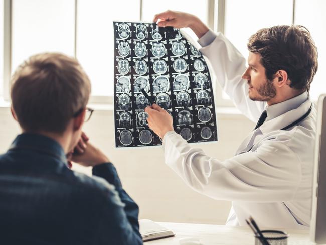 Gold Coast Suns - My Life - Tasman Oncology Research.Handsome young doctor in white coat is showing x-ray image to his patient while working in office