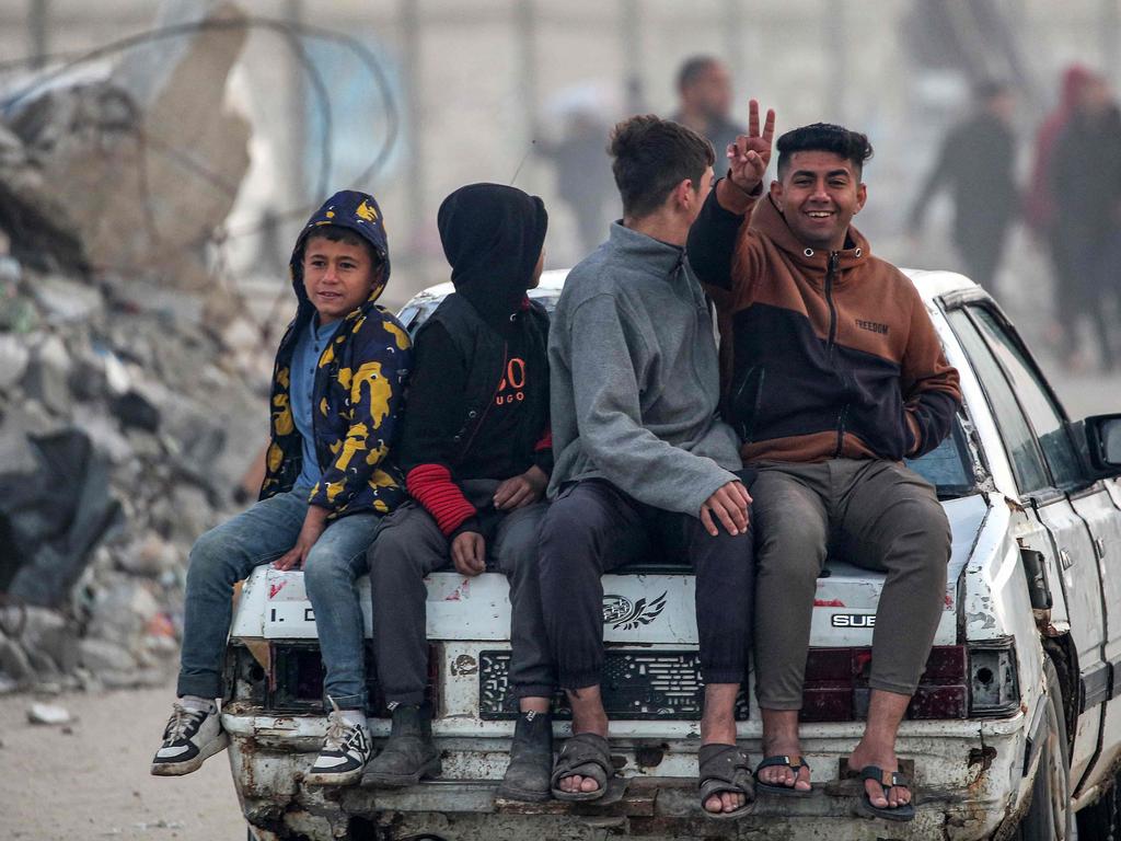 A youth gestures while sitting with other children on the boot of a moving vehicle as people gather along the Salah al-Din road in Nuseirat, January 27, 2025. Picture: AFP