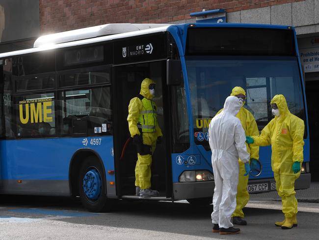 Members of Spanish Military Emergencies Unit (UME), wearing protective suits, stand outside a bus used to transport patients from the San Carlos Clinic Hospital to a temporary hospital set-up for coronavirus patients at the Ifema convention and exhibition centre in Madrid. Picture: AFP