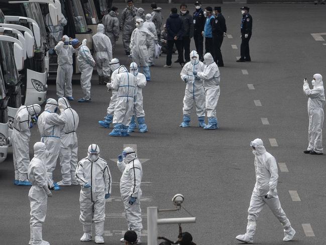 Chinese workers and health officials wear protective white suits as they wait for travellers from Wuhan. Picture: Getty