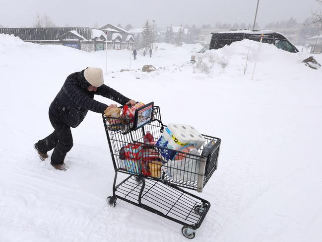 A customer pushes their grocery cart through the snow to their car as a blizzard hits Mammoth Lakes, California. Picture: David Swanson/AFP