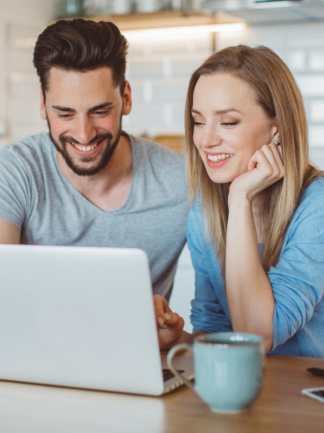 Young couple doing their finances at home. They are wearing pajamas and drinking first coffee of the day at the kitchen.