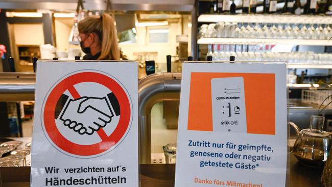 Signs reading 'We disclaim handshakes' (L) and 'Access only for persons who are vaccinated, recovered or have a negative test' are seen on the counter of a restaurant in Ludwigsburg, southwestern Germany. Picture: AFP