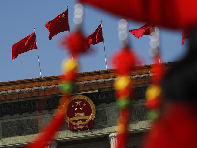 China national flag flutters near the national emblem is seen through a bus usher in ethnic minority costume during the opening session of China's National People's Congress at the Great Hall of the People in Beijing, Tuesday, March 5, 2019. China's government announced a robust annual economic growth target and a 7.5 percent rise in military spending Tuesday at a legislative session overshadowed by a tariff war with Washington. (AP Photo/Andy Wong)