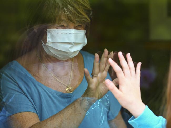 Grandmother and granddaughter touch hands on window during the lockdowns.