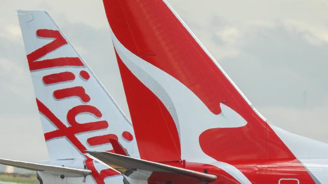 The vertical stabilisers of a Qantas Boeing B737-838 plane, registration VH-VZQ, and a Virgin Australia Boeing B737-8FE plane, registration VH-VUZ, waiting at the northern end of the main runway of Sydney Kingsford-Smith Airport in preparation for departure.  The Qantas plane is heading to Adelaide as flight QF741 and the Virgin plane is heading to Adelaide as flight VA428.  In the background is another Virgin B737-8FE plane. This image was taken from Nigel Love Bridge, Mascot on a sunny afternoon on 3 December 2023.