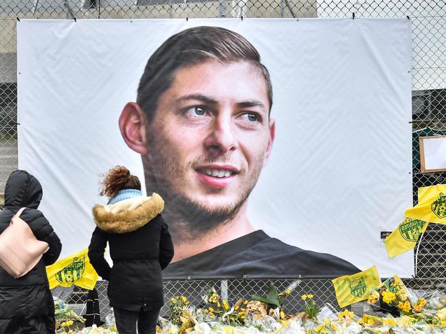 People look at yellow flowers displayed in front of the portrait of Argentinian forward Emiliano Sala at the Beaujoire stadium in Nantes, on February 8, 2019. - FC Nantes football club announced on February 8, 2019 that it will freeze the #9 jersey as a tribute to Cardiff City and former Nantes footballer Emiliano Sala who died in a plane crash in the English Channel on January 21, 2019. (Photo by LOIC VENANCE / AFP)