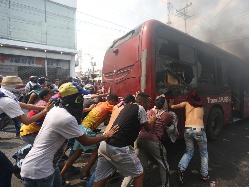 Demonstrators push away a bus that was torched during clashes with the Bolivarian National Guard, heightening tensions over blocked humanitarian aid. Picture: AP Photo/Fernando Llano