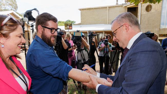 Prime Minister Anthony Albanese writes and signs ‘No Change To WA GST’ on the forearm of Dylan Caporn, State Political reporter for The West Australian before signing a copy of The West Australian newspaper. (AAP Image/Richard Wainwright)