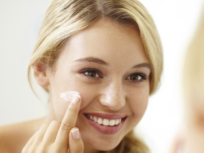 Pretty young woman smiling while applying face cream to her skin cb