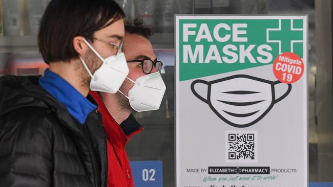 People wearing face masks walk past a sign advertising masks in Melbourne on July 20, 2020. Photo by William WEST/AFP