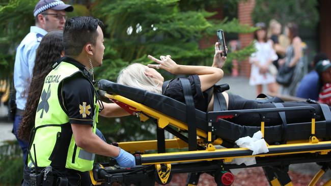 A girl takes a selfie as she is taken away on a stretcher outside the Rolling Loud Festival on Sunday. Picture: Damian Shaw