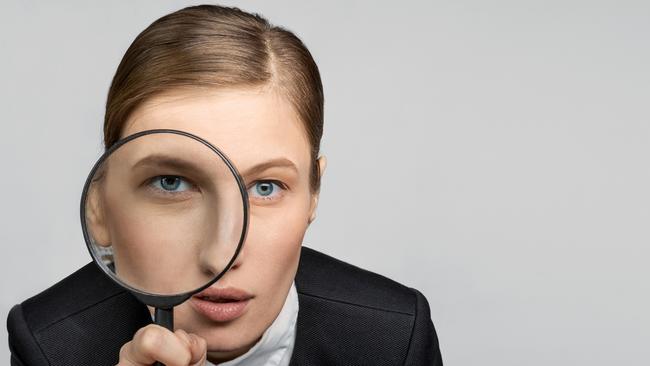 Portrait of a girl in the office at work looks carefully into the magnifying glass with one eye. The concept of office work and search. tax generic