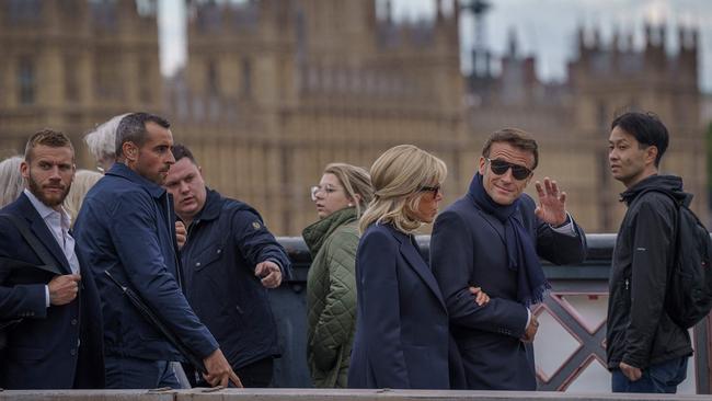 French President Emmanuel Macron waves as he and his wife Brigitte Macron walk along a bridge with the Palace of Westminster in the background in London on September 18, on the eve of the funeral of Queen Elizabeth II.