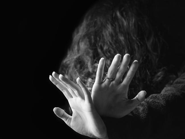 Concept of a violence against women. Black and white portrait of scared and desperate woman, focus on the hands in protective gesture