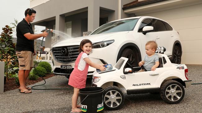 Ryan Allen with his children Hudson, 1, and Ava, 3, using grey recycled water to wash their cars at their home. Picture: Jonathan Ng