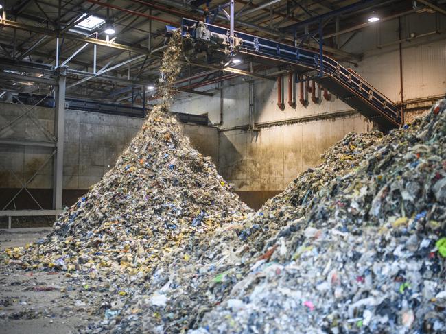 Floor-level action shot of separated recyclables falling from elevated conveyor belt onto growing pile inside waste management facility.